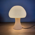 Mushroom table lamp with rippled shade glowing warmly on a nightstand